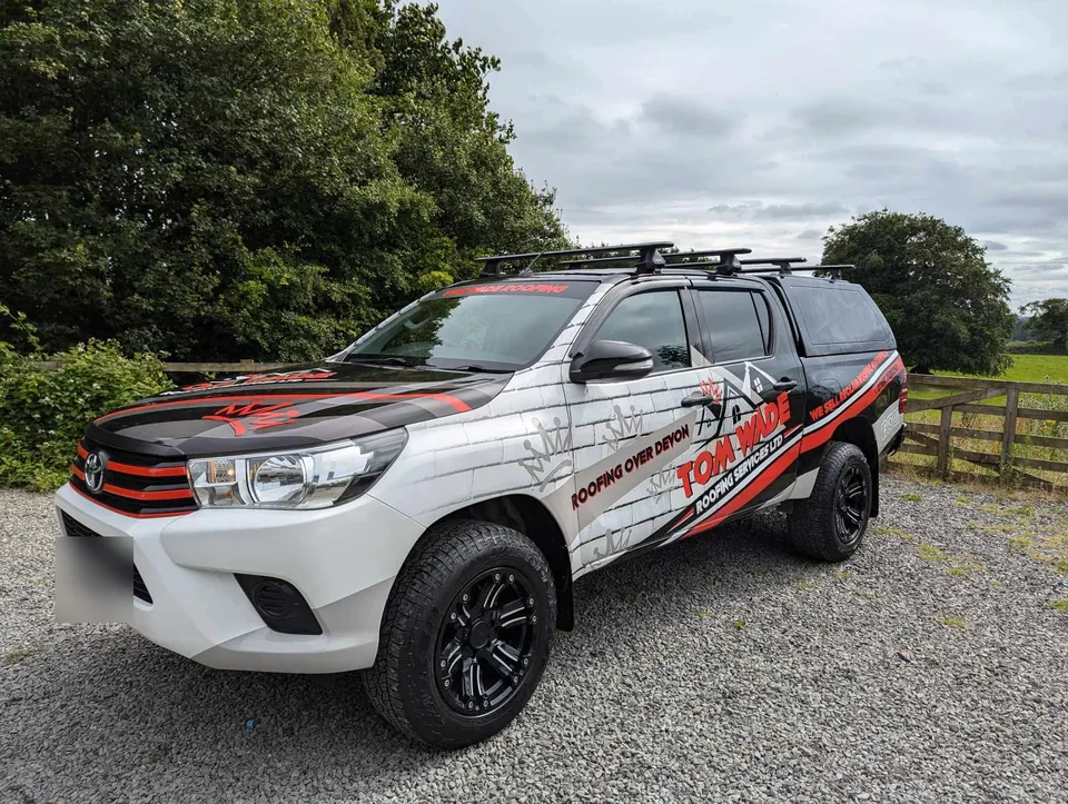 Tom Wade Roofing Services Hilux pickup in its red, black and white Roofing over Devon wrap